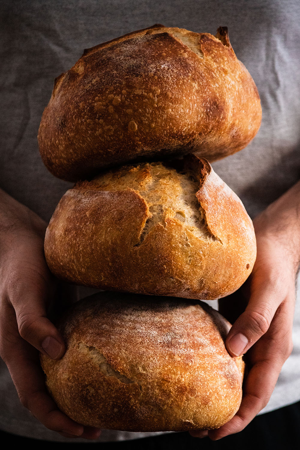 Man's hands holding three loaves of artisan bread.