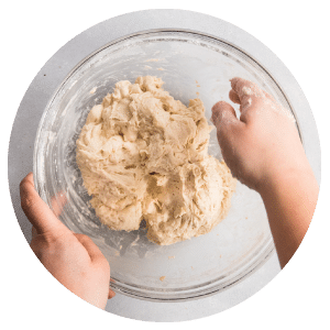 hands mixing bread dough in a glass bowl